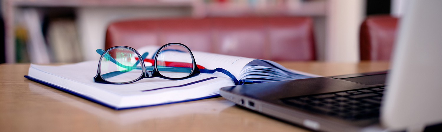 Glasses and Open Book in Front of Laptop